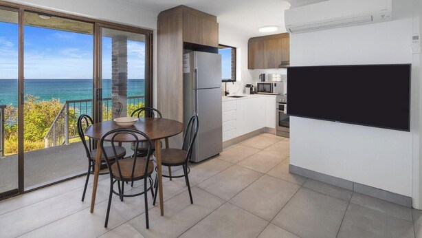 Uma cozinha moderna com uma televisão grande, uma área de refeições com vista para o mar e uma varanda com mesa e cadeiras.