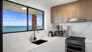 Uma cozinha com vista para o oceano, uma chaminé de tijolos, um exaustor de aço inoxidável, um micro-ondas e um fogão.