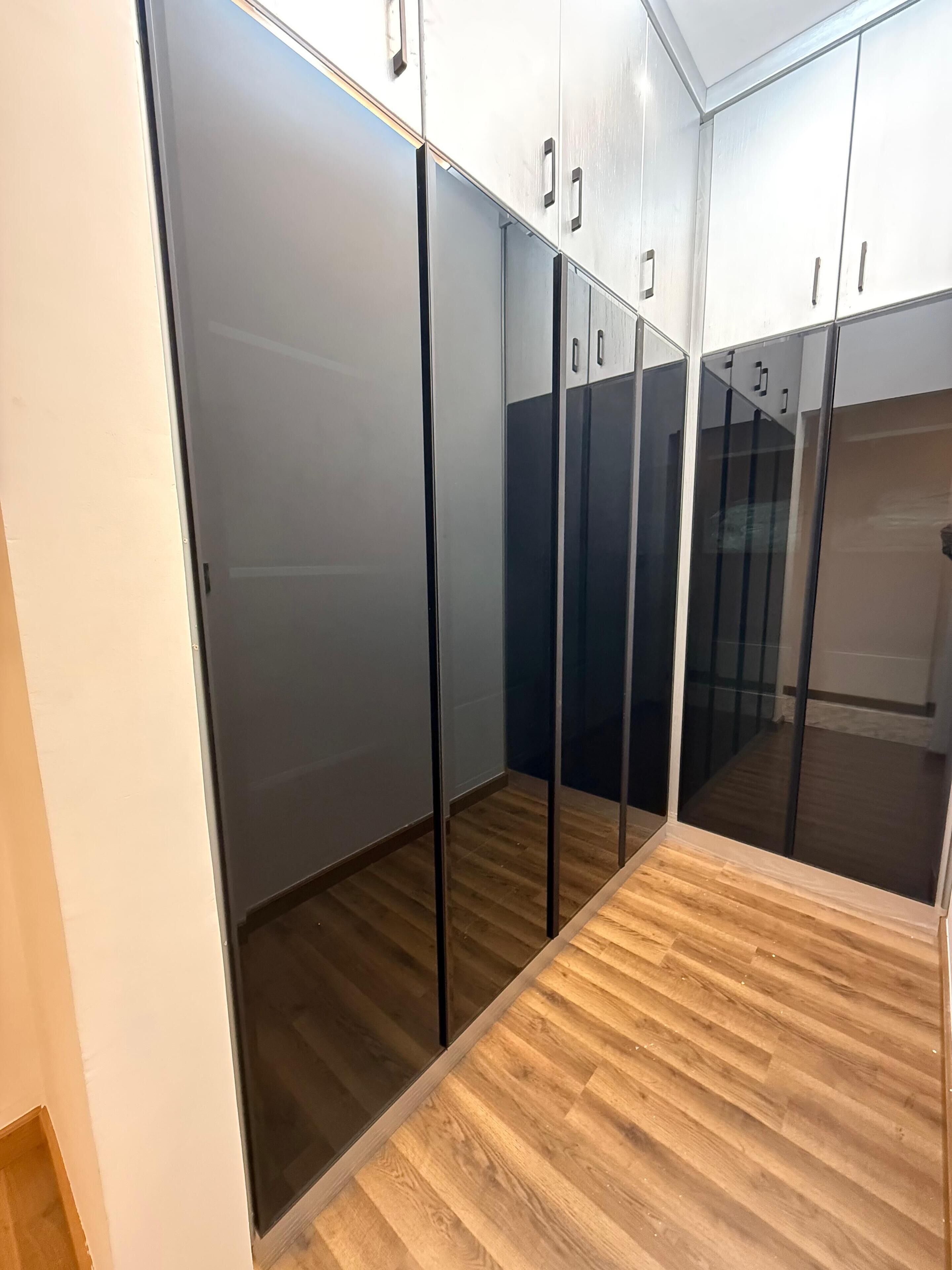 A modern, enclosed closet with mirrored doors and a wooden floor.