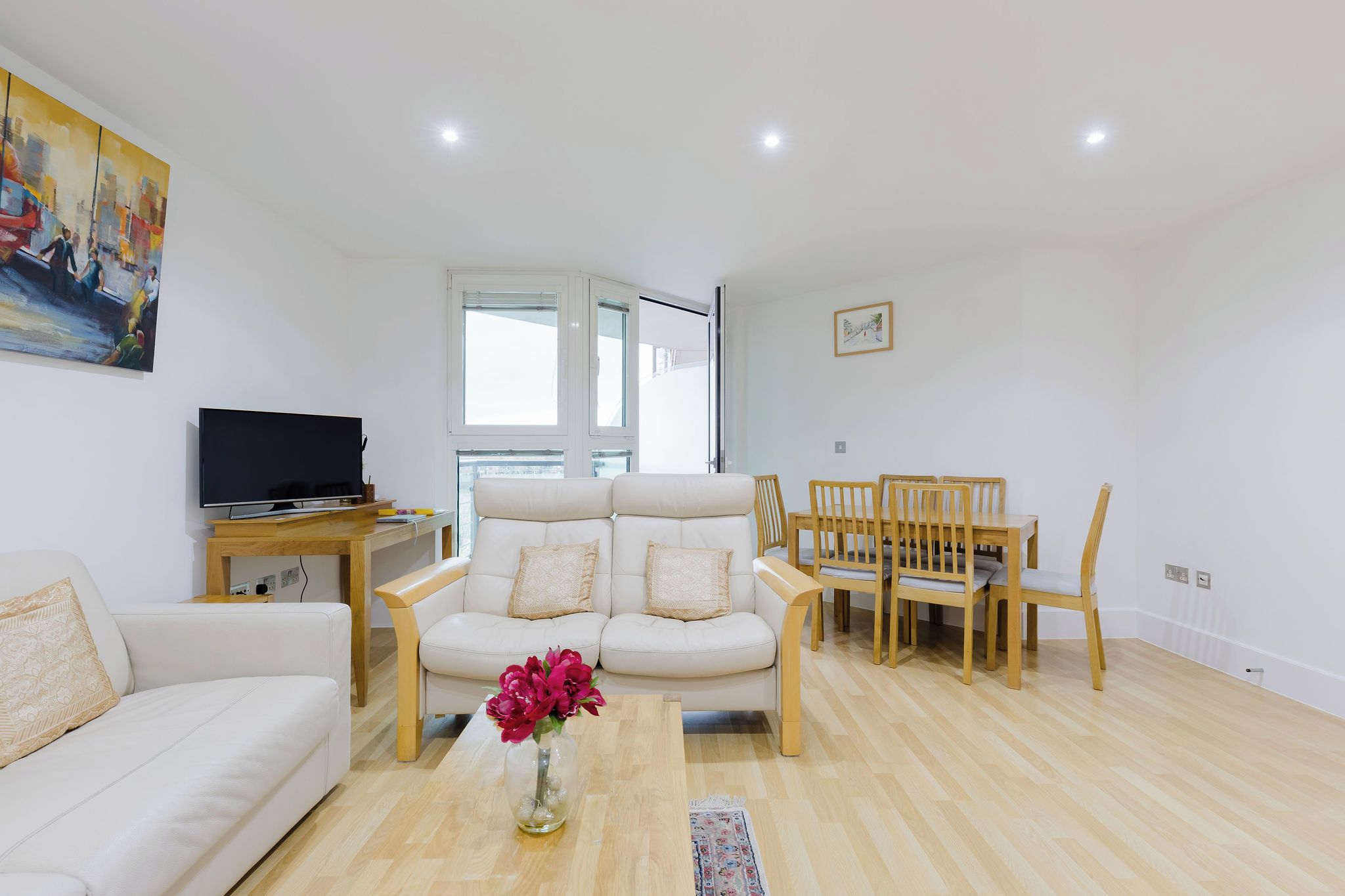 A modern living room with a sofa, a dining table with chairs, a TV, and a painting on the wall.