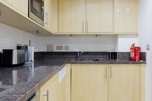 A kitchen with wooden cabinets, a granite countertop, a stainless steel range hood, a built-in microwave, a sink, and a fire extinguisher. - Welcoming 2BDR Riverside Retreat in Central London (Greater London)