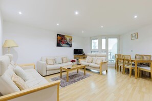 A modern living room with a sofa, a coffee table, and a dining area with chairs. - Welcoming 2BDR Riverside Retreat in Central London (Greater London)