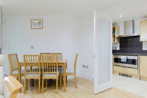 A modern kitchen with a built-in oven and a dining area with wooden chairs and a table. - Welcoming 2BDR Riverside Retreat in Central London (Greater London)