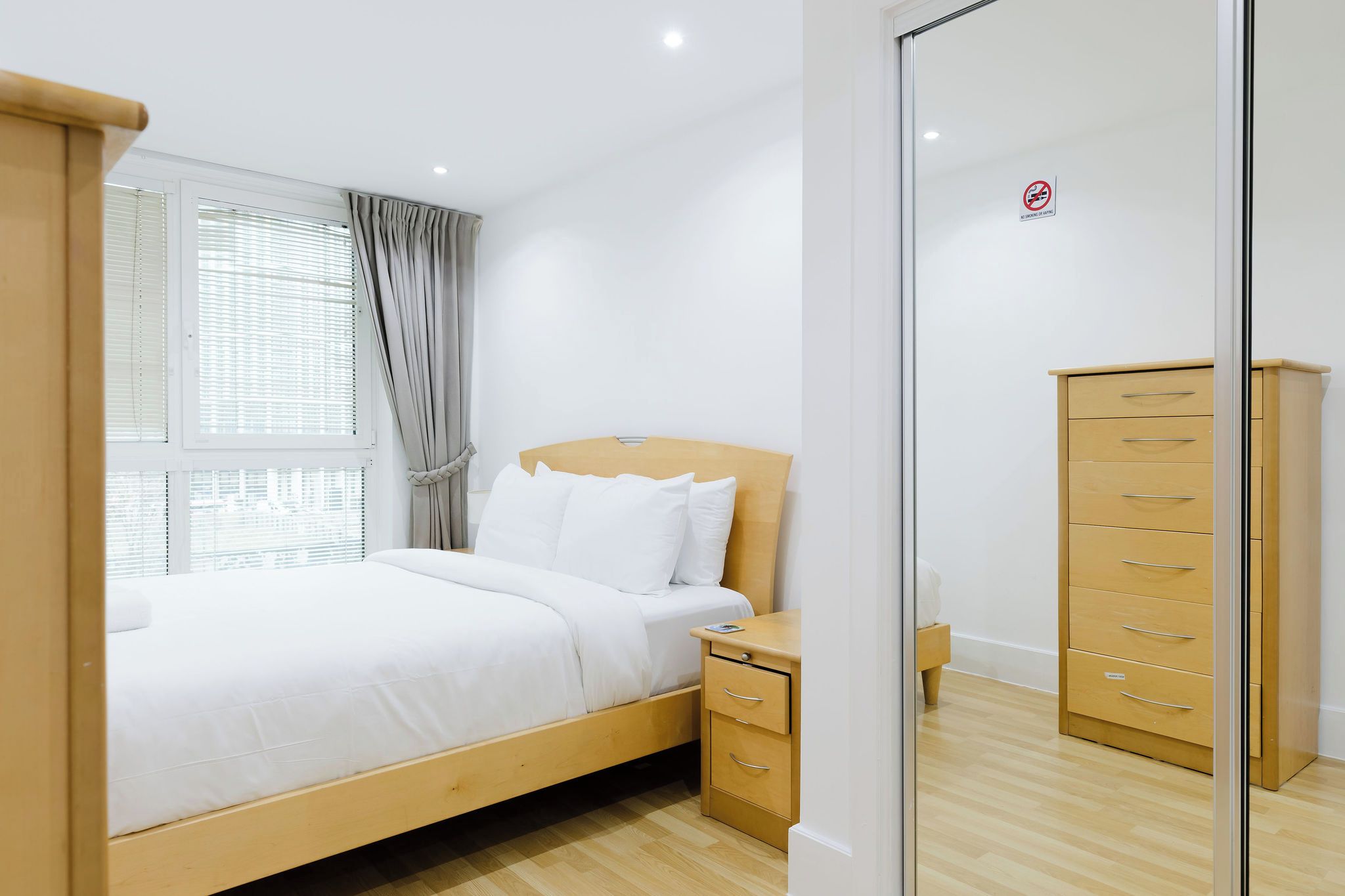 A modern bedroom with a wooden bed, a bedside table, a wardrobe, and a glass partition.