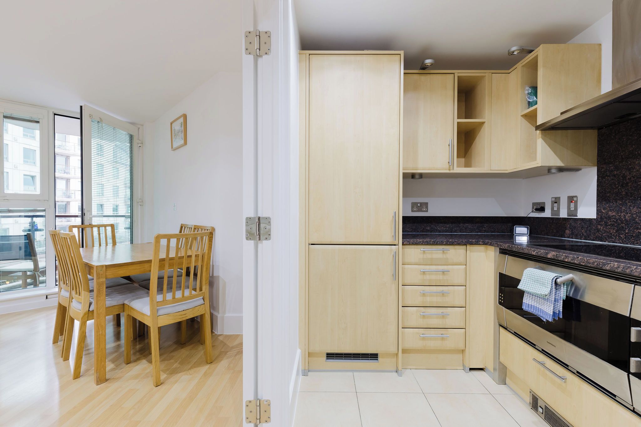 Une cuisine moderne avec des meubles en bois, une table à manger avec des chaises et une grande fenêtre.
