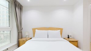 Ein Hotelzimmer mit einem Einzelbett, zwei Nachttischen, einer Lampe, einem Telefon und einem Fenster mit Jalousien.