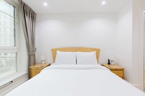 A hotel room with a single bed, two bedside tables, a lamp, a phone, and a window with blinds. - Welcoming 2BDR Riverside Retreat in Central London (Greater London)
