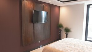 Une chambre à coucher avec un grand lit, un téléviseur à écran plat fixé sur un mur recouvert de panneaux en bois, et une plante en pot placée à côté du lit.