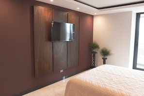 A bedroom with a large bed, a flat-screen TV mounted on a wooden panel wall, and a potted plant beside the bed. - Siena: Bright and modern 2-bedroom apartment (Santa Cruz de la Sierra)