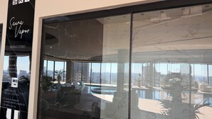 Un intérieur moderne avec une grande baie vitrée qui reflète une piscine et le paysage urbain.