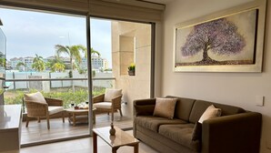 Ein modernes Wohnzimmer mit einem großen Schiebeglasfenster, das auf einen Balkon führt, ein braunes Sofa, zwei Korbstühle und ein kleiner Holztisch.