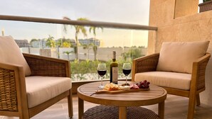 Ein Balkon mit Korbstühlen und einem runden Tisch, ausgestattet mit einer Weinflasche, Gläsern und einer Käseplatte.