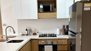 Eine moderne Küche mit weißen Schränken, einem Edelstahl-Kühlschrank, einer Mikrowelle, einem Gasherd und einem Einbauofen.