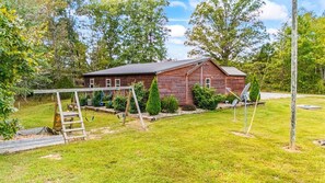 A rustic wooden cabin with a fenced yard, a swing set, and satellite dishes. - Fabulous 2-bedroom cabin near Mammoth Cave (Cub Run)
