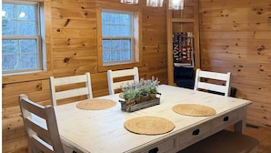 Interno di una baita in legno con un tavolo da pranzo, sedie, una panca, un lampadario e finestre.