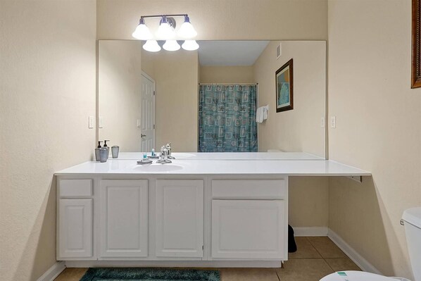 Un baño con tocador blanco, un espejo grande y una cortina de ducha estampada.