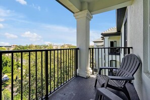 Uma varanda com vista para uma área residencial, um pilar branco e duas cadeiras Adirondack.