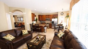 A living room with two brown leather sofas, a coffee table, and a dining area with wooden chairs and a kitchen in the background. - 2540 Windsor Hills (Kissimmee)