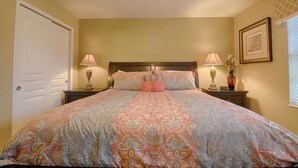 A bedroom with a large bed, two bedside tables with lamps, a door, and a framed picture on the wall. - 2540 Windsor Hills (Kissimmee)