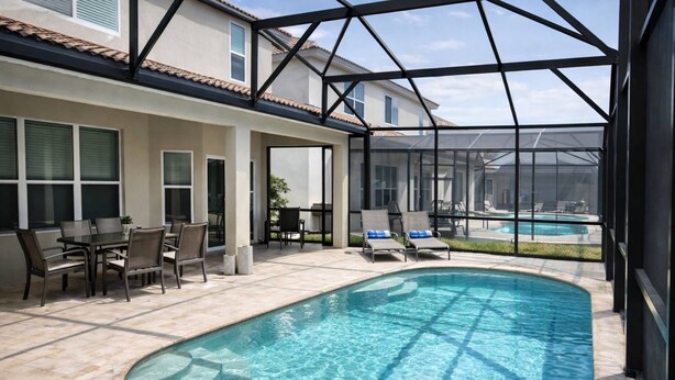 A swimming pool with a glass enclosure, a patio with chairs and a table, and a view of a house in the background. - 2540 Windsor Hills (Kissimmee)