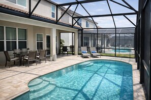 A swimming pool with a glass enclosure, a patio with chairs and a table, and a view of a house in the background. - 2540 Windsor Hills (Kissimmee)