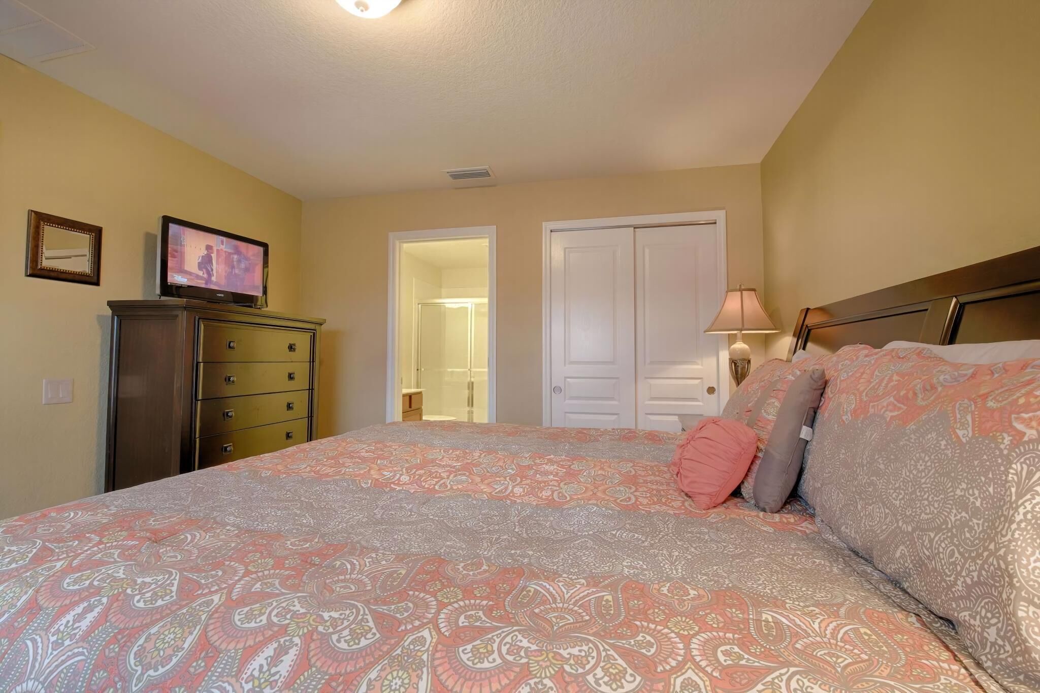 Un dormitorio con cama, cómoda, televisor y puerta que da a otra habitación.