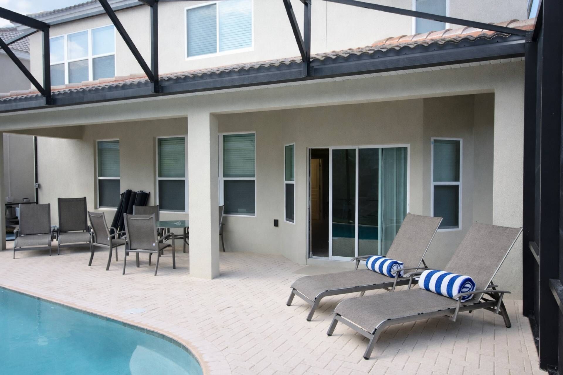 A poolside area with lounge chairs and a table, a covered patio with chairs, and a building with windows and a door.