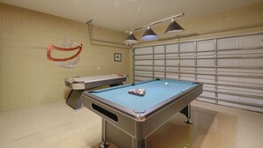 A pool table with a blue felt surface, a red and white pool cue, and three hanging lamps. - 2540 Windsor Hills (Kissimmee)