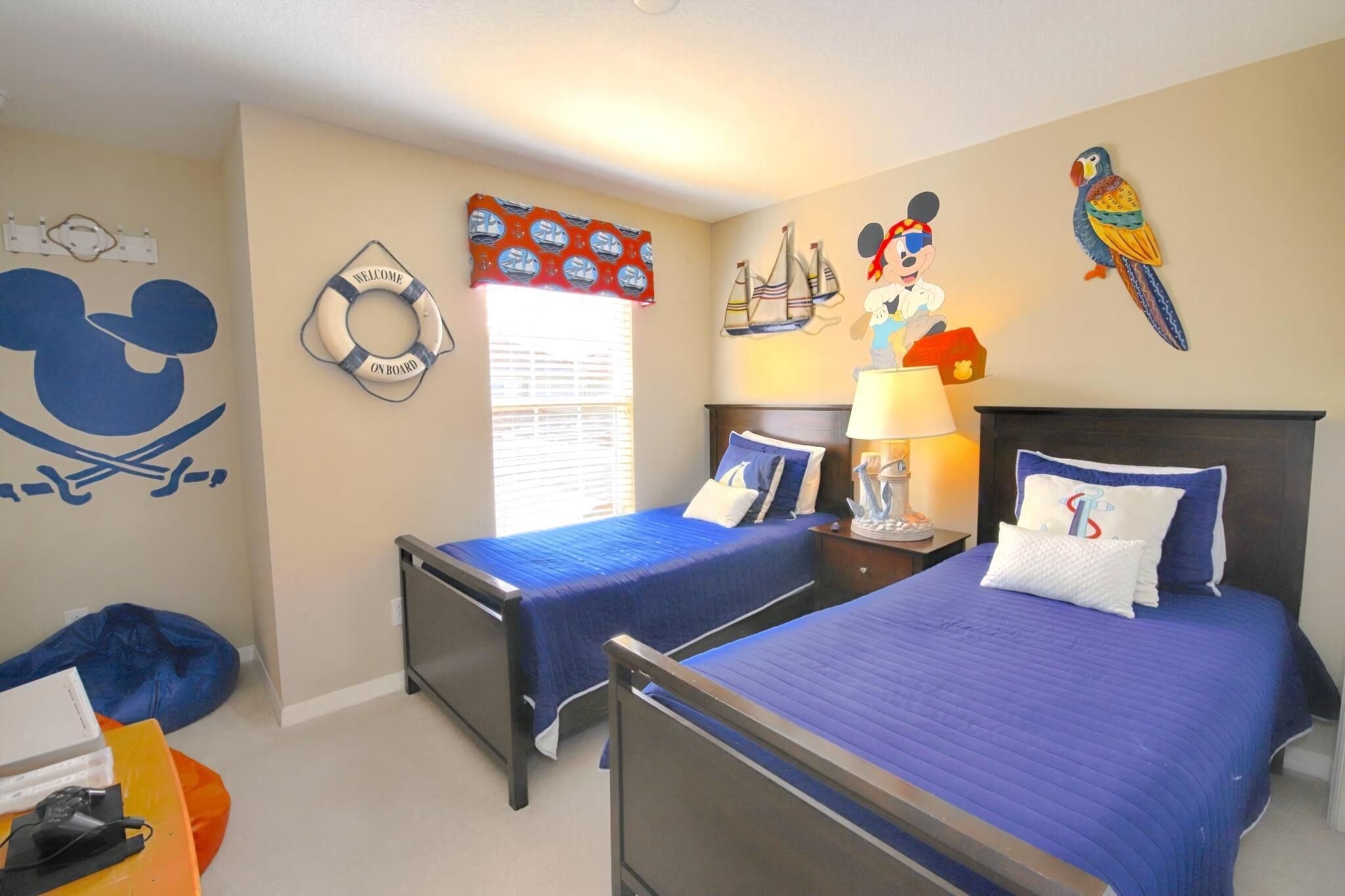 Une chambre d’hôtel avec deux lits, une fresque représentant Mickey Mouse, une décoration en forme de bouée de sauvetage, un panneau d’accueil et une décoration murale représentant un perroquet.