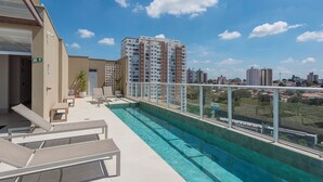 A rooftop pool with lounge chairs and a view of surrounding buildings. - Cozy Studio in Cambuí (Campinas)