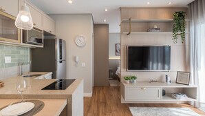A modern kitchen with an island, built-in appliances, and a large TV. - Cozy Studio in Cambuí (Campinas)