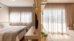 A modern hotel room with a bed, a desk, a TV, and a sofa. - Cozy Studio in Cambuí (Campinas)