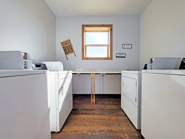A laundry room with two white washing machines, a wooden table, a window, and a wall-mounted laundry sign.