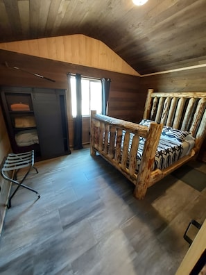 A wooden interior with a bed, a chair, a wardrobe, and a window.