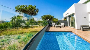Un área de piscina exterior moderna con una vista despejada del cielo, una terraza de madera y un espacio de descanso con sillas y una mesa.