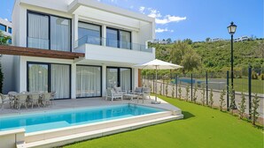 Una casa moderna de dos pisos con piscina, mobiliario exterior y vista a un paisaje montañoso.