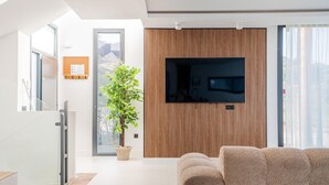 Una sala de estar moderna con un televisor de pantalla plana montado en una pared de paneles de madera, una planta en maceta y un sofá color beige.
