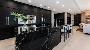A modern kitchen with a black marble island, stainless steel appliances, and a potted plant. - Aqua 4 on Seven Mile Beach (Seven Mile Beach)