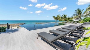 A poolside area with lounge chairs, a clear view of the ocean, and a tropical setting with palm trees. - Aqua 4 on Seven Mile Beach (Seven Mile Beach)