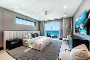 A modern hotel room with a large bed, a TV, a desk, and a view of the ocean. - Aqua 4 on Seven Mile Beach (Seven Mile Beach)