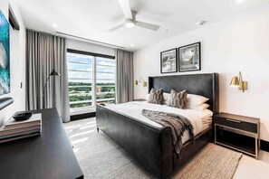Una habitación de hotel moderna con una cama grande, un escritorio con una laptop, una lámpara de pie y vistas a la ciudad.