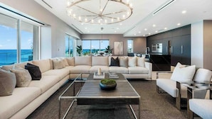 A modern living room with a large sectional sofa, a coffee table, and a kitchen area in the background. - Aqua 4 on Seven Mile Beach (Seven Mile Beach)
