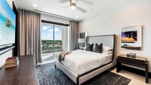 A modern hotel room with a large bed, a ceiling fan, a TV, and a view of the city. - Aqua 4 on Seven Mile Beach (Seven Mile Beach)