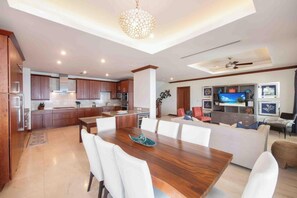 A modern kitchen with wooden cabinets, a dining area with a wooden table and white chairs, and a living area with a sofa and TV. - Casa Luna (George Town)