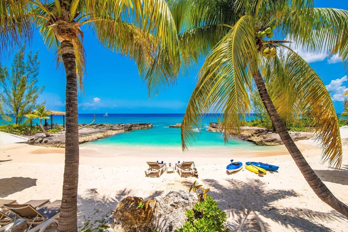 A beach with palm trees, clear turquoise water, and a few boats.