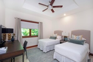 A hotel room with two beds, a desk, a ceiling fan, a window with curtains, and a view of greenery outside. - Casa Luna (George Town)
