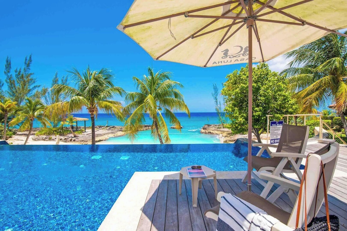 A poolside area with a view of the ocean, palm trees, and a sign indicating pool rules.