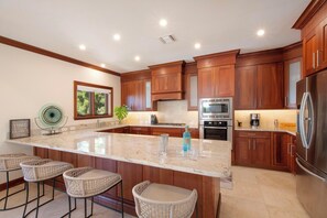 A modern kitchen with wooden cabinets, a large island, bar stools, and stainless steel appliances. - Casa Luna (George Town)