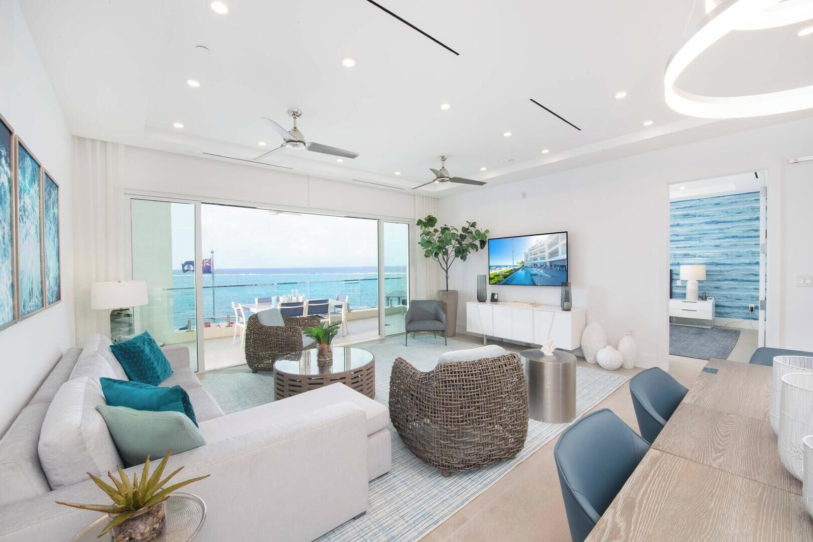 A modern living room with a sofa, chairs, a TV, and a balcony with a view of the sea.