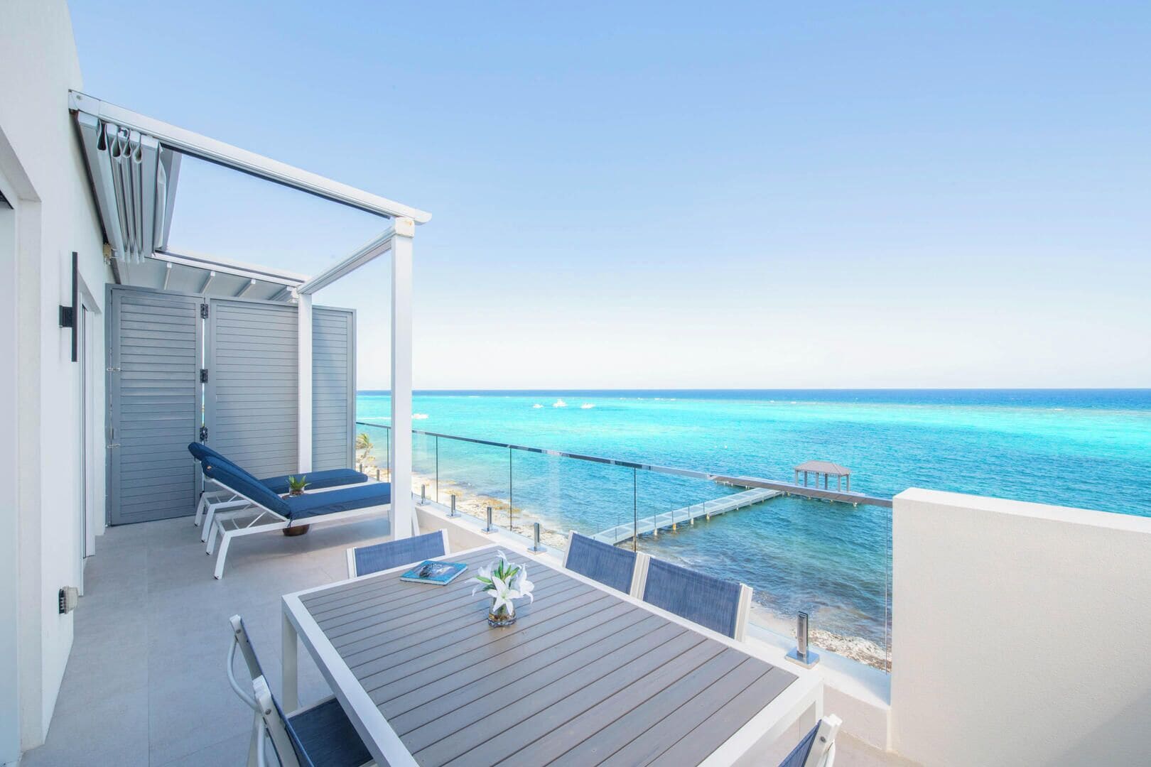 Un balcon avec vue sur l’océan, une table et des chaises longues.
